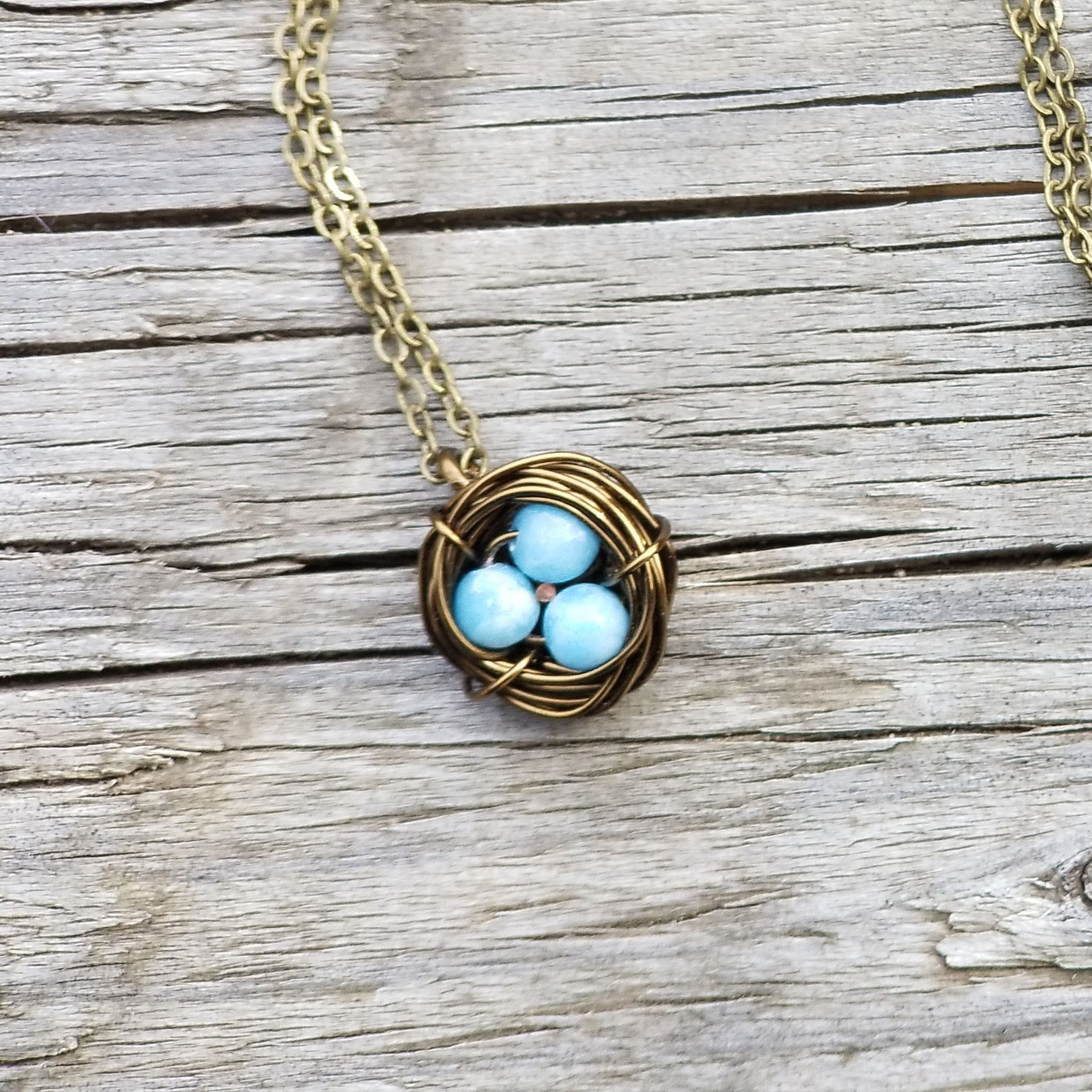 pendant with brass finish in shape of a bird's nest with three blue beads inside resembling robin's eggs 
