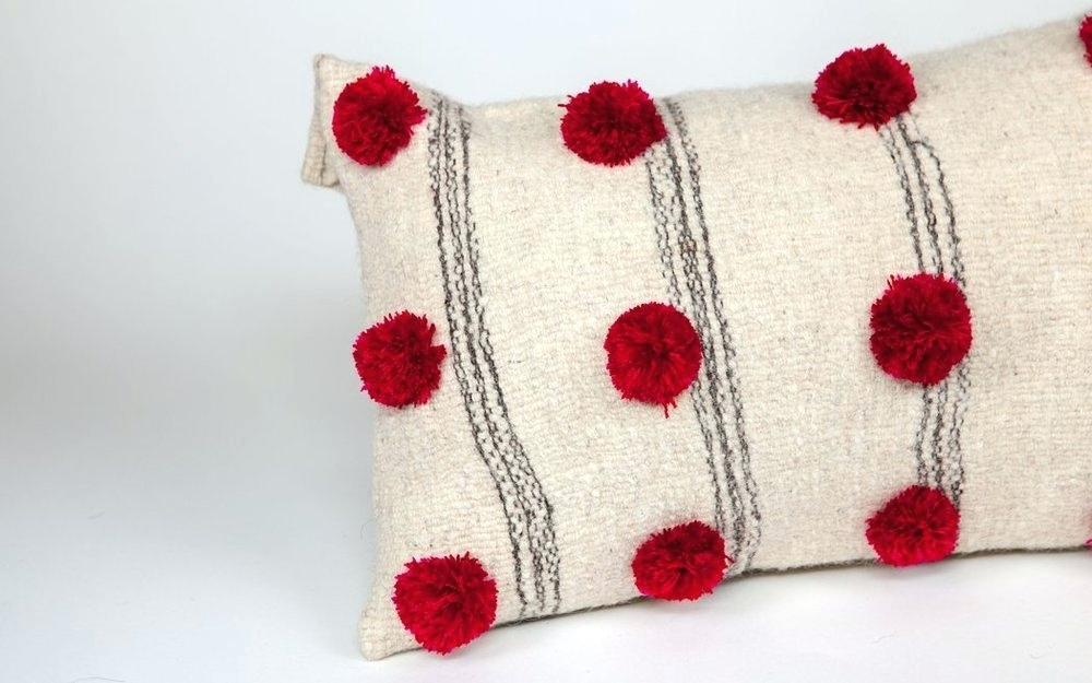 white pillow with black stripes and red pompoms 