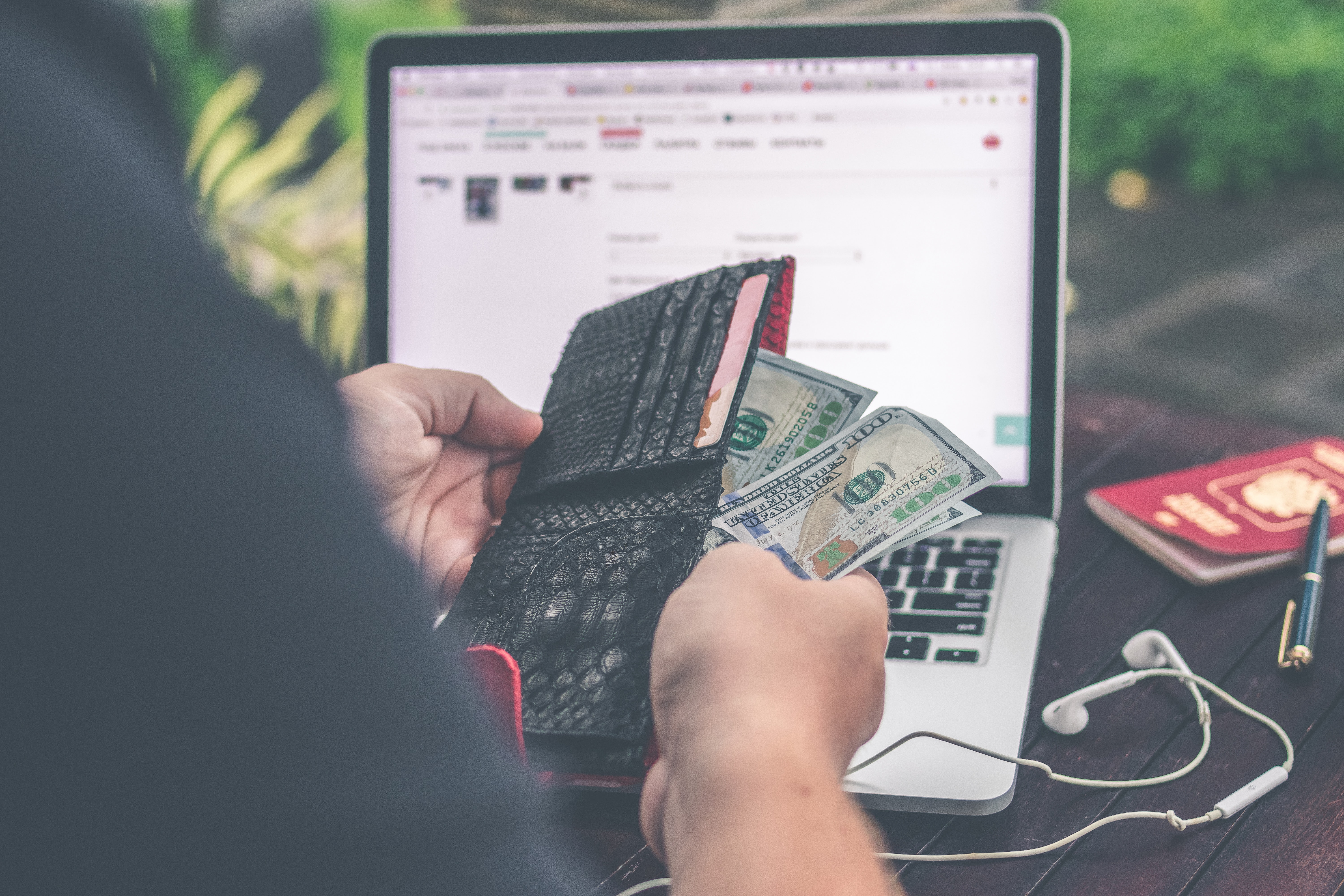 person holding money in front of laptop